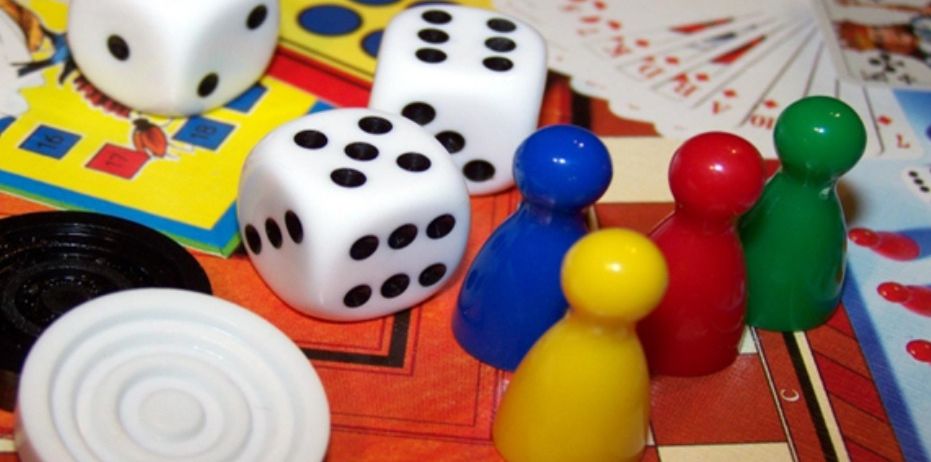 Ein Brettspiel mit verschiedenen Teilen, einschließlich Würfel, Karten und Figuren in verschiedenen Farben, ist auf einem Tisch aufgebaut.