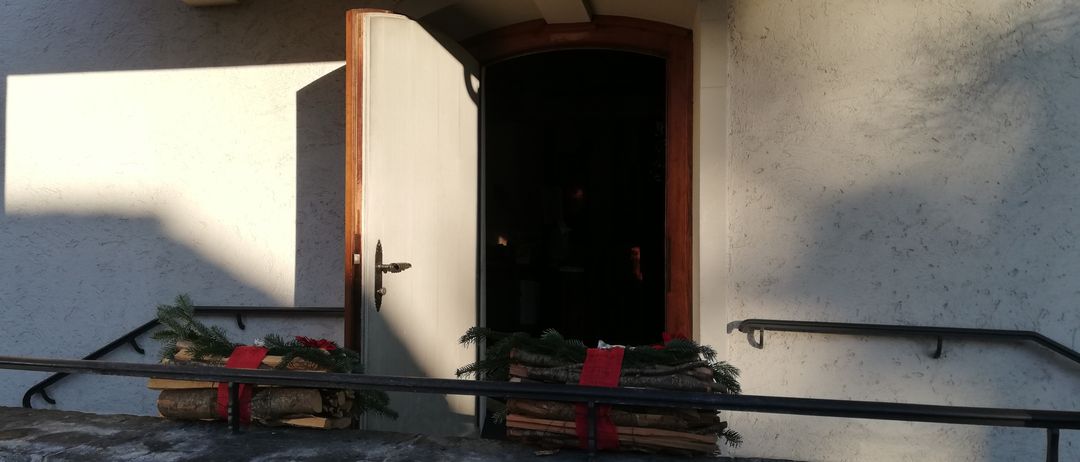 Ein Gebäude mit einer offenen Tür auf einem Balkon, mit Holzscheiten, die mit roten Bändern zusammengebunden sind, und einem Blick ins dunkle Innere.