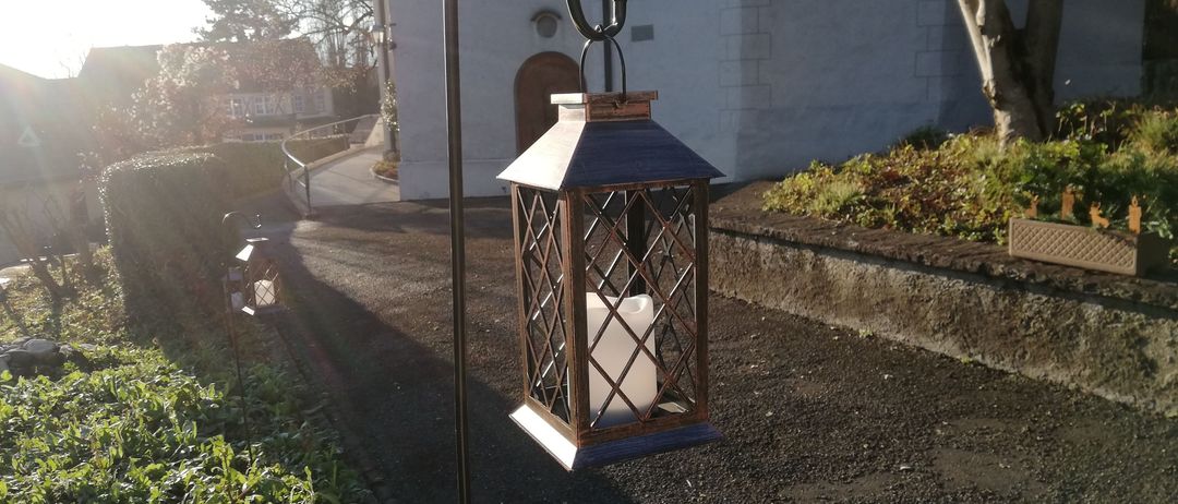 Eine Laterne mit einer Kerze darin hängt an einem Pfosten vor einer Kirche.