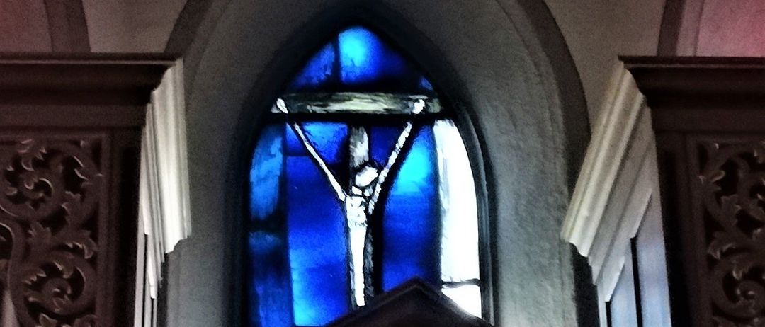 Ein Kirchenfenster mit einem Kreuz, blauem Buntglas und einem Holzrahmen.