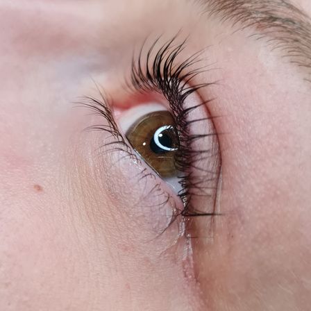 Nahaufnahme eines Augens mit langen Wimpern, das eine braune Iris und eine sichtbare Tränenlinie zeigt.