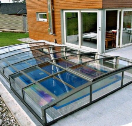 Ein modernes Haus mit einem Glasschwimmbad, das von einem Glasvordach auf der Terrasse bedeckt ist.