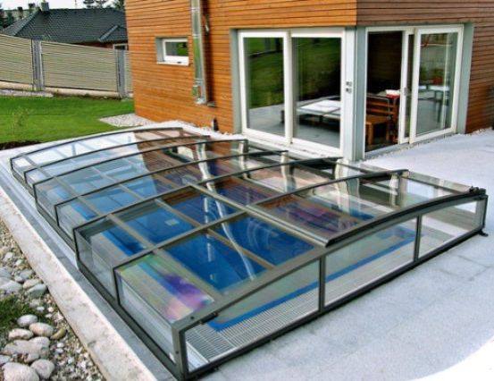 Ein modernes Haus mit einem Glasschwimmbad, das von einem Glasvordach auf der Terrasse bedeckt ist.