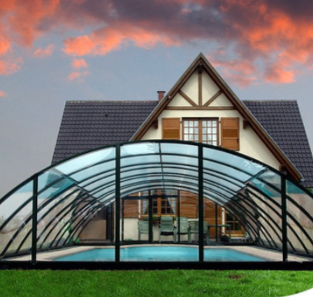 Ein modernes Haus mit einer Glaspoolabdeckung steht vor einem bunten Himmel. Das Haus verfügt über ein Giebeldach und braune Fensterläden.