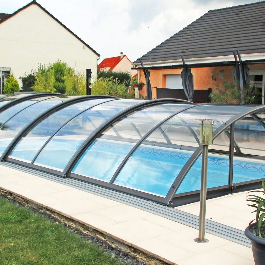 Ein Außenpool mit einem Glasdach, der sich im Garten befindet. Das Haus hat ein graues Dach und eine orange Wand.