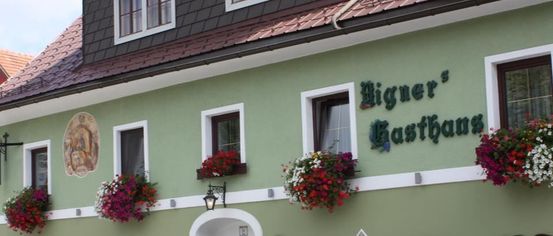 Ein traditionelles grünes Gebäude mit rotem Dach und weißen Begrenzungen. Es hat viele Fenster und einen dekorativen Eingang mit hängenden Blumen.
