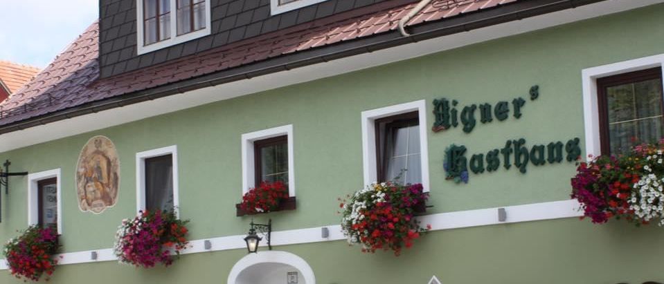 Ein traditionelles grünes Gebäude mit rotem Dach und weißen Begrenzungen. Es hat viele Fenster und einen dekorativen Eingang mit hängenden Blumen.