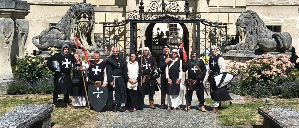 Eine Gruppe von Menschen in mittelalterlichen Kostümen posiert für ein Foto vor einem verzierten Tor.