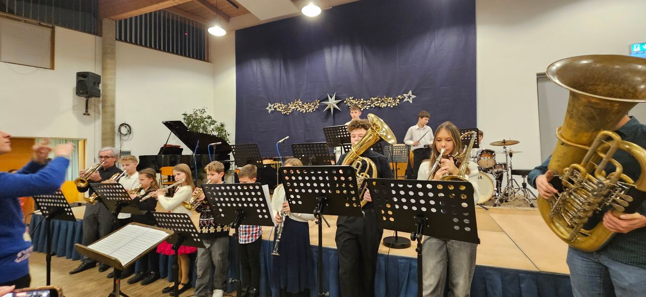 Mehrere Kinder stehen mit Musikinstrumenten auf einer Bühne in einem Raum mit blauem Vorhang und Sternendekoration.