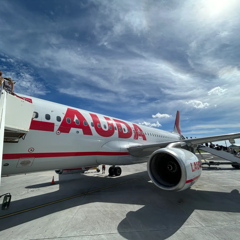 Ein weißes Flugzeug mit roten Akzenten und dem Wort 'Auda' auf der Seite ist auf dem Vorfeld geparkt.