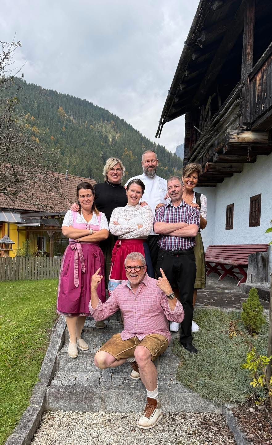 Eine Gruppe von sechs Personen posiert für ein Foto vor einem Haus mit Bergen im Hintergrund.
