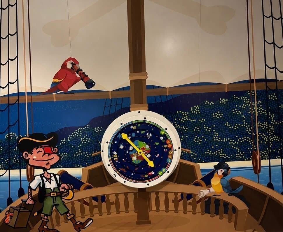 Innenraum eines Piratenschiffs mit einem großen Kompass und einem Papagei. Ein Piratenjunge steht neben dem Kompass, während ein Papagei auf einer Brüstung sitzt.