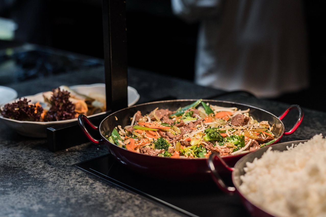 Eine Nahaufnahme eines roten Woks mit Gebratenem Rindfleisch und Gemüse auf einem Herd.