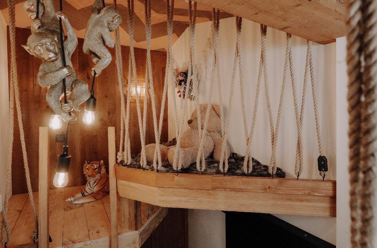 A cozy children's room with a wooden bunk bed, ropes, and a stuffed bear on a bed with fur. A tiger toy lies on the floor.