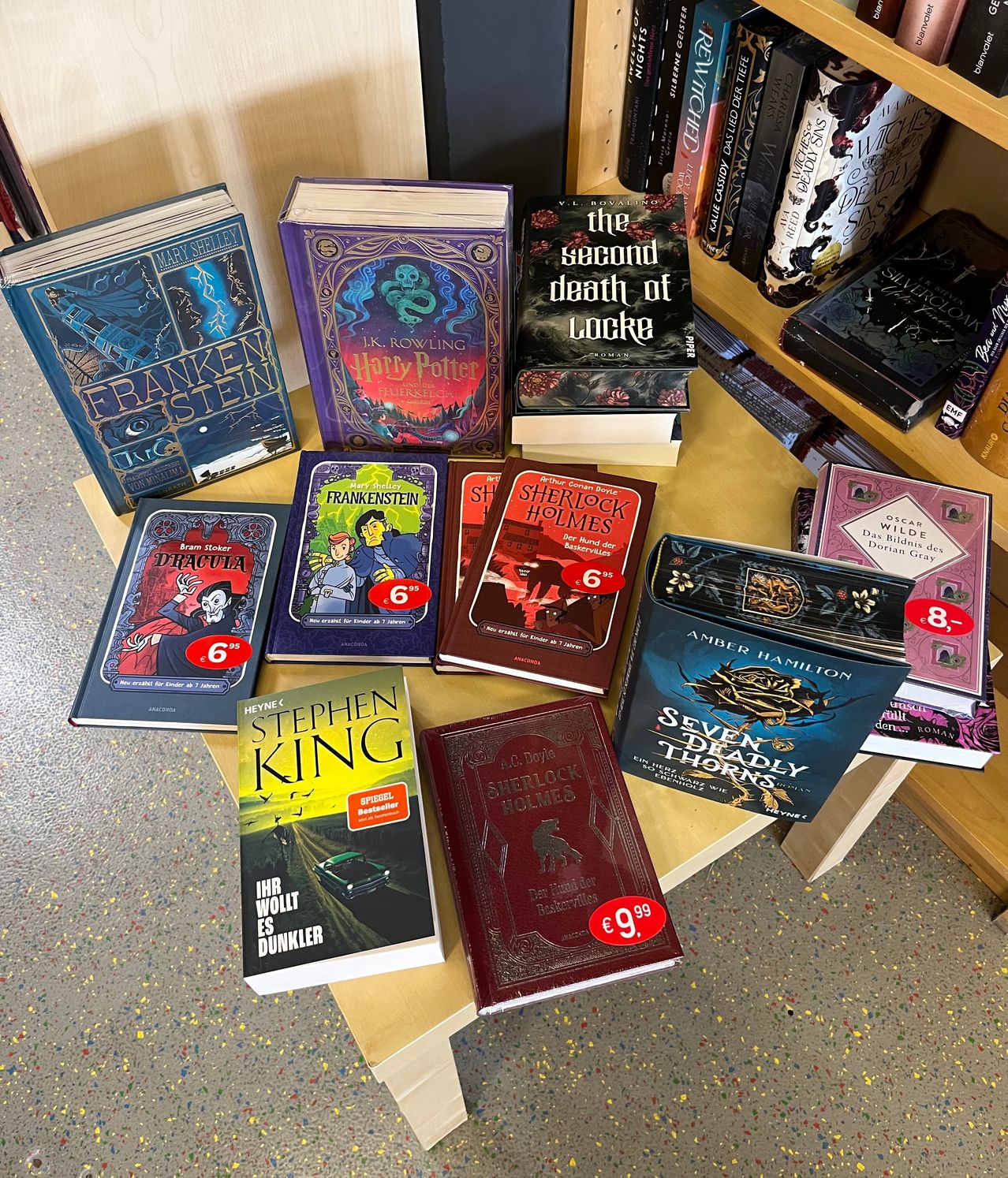Eine Sammlung von Büchern auf einem Holztisch, darunter Frankenstein, Dracula, Harry Potter, Sherlock Holmes und andere, zum Preis von 6 und 9,99 Euro.