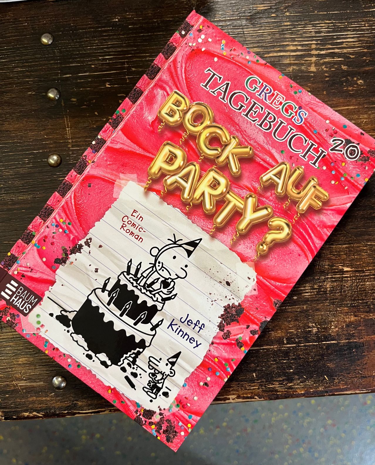 Ein rosa Buch mit dem Titel Gregs Tagebuch: Rock auf Party 20. Das Cover zeigt einen Geburtstagskuchen mit goldenen Luftballons und Streuseln.