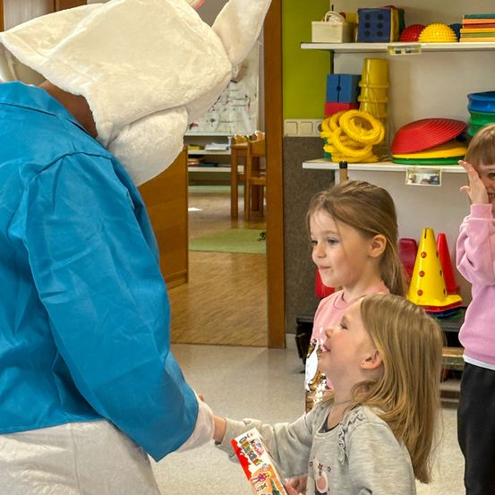 Eine Person in einem Kostüm gibt einem Kind in einem Raum mit Spielzeugregalen ein Geschenk.