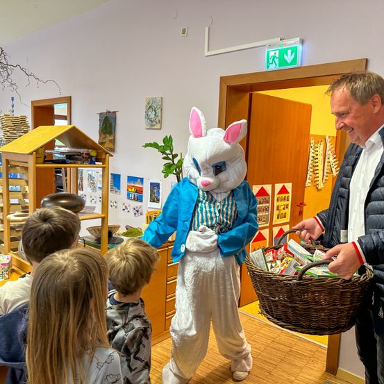 Eine Person in einem Hasenkostüm verteilt Osterkörbe an Kinder.