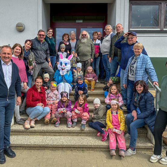 Eine Gruppe von Erwachsenen und Kindern posiert auf den Stufen eines Gebäudes für ein Foto. Eine Person in einem Hasenkostüm steht in der Mitte.