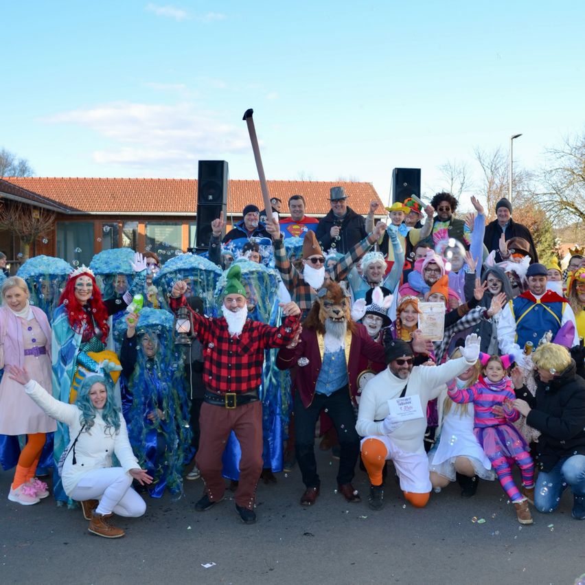 Eine große Gruppe von Menschen in verschiedenen Kostümen, darunter ein Zauberer, eine Meerjungfrau und ein Pirat, posiert für ein Foto vor einem Gebäude.