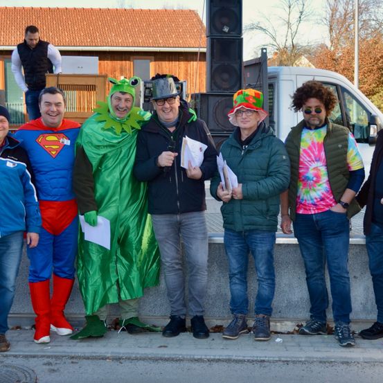 Eine Gruppe von Männern in verschiedenen Kostümen posiert für ein Foto vor einem Gebäude mit rotem Dach.