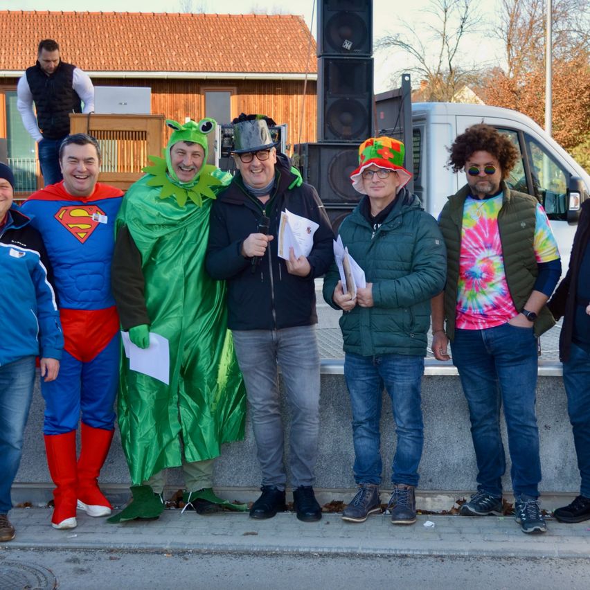 Eine Gruppe von Männern in verschiedenen Kostümen posiert für ein Foto vor einem Gebäude mit rotem Dach.