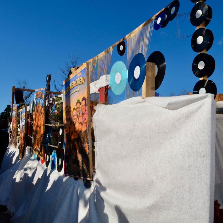 Ein weißer Hintergrund mit mehreren Postern und aufgehängten Schallplatten, darunter eine blaue, unter einem klaren blauen Himmel.