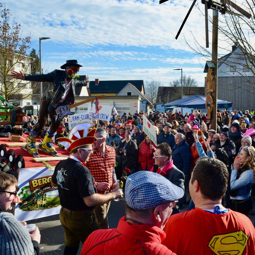 Eine Menschenmenge bei einer Veranstaltung im Freien, ein Mann auf einer Bühne tritt auf, andere halten Schilder und jubeln, mit Bannern und feierlicher Atmosphäre.