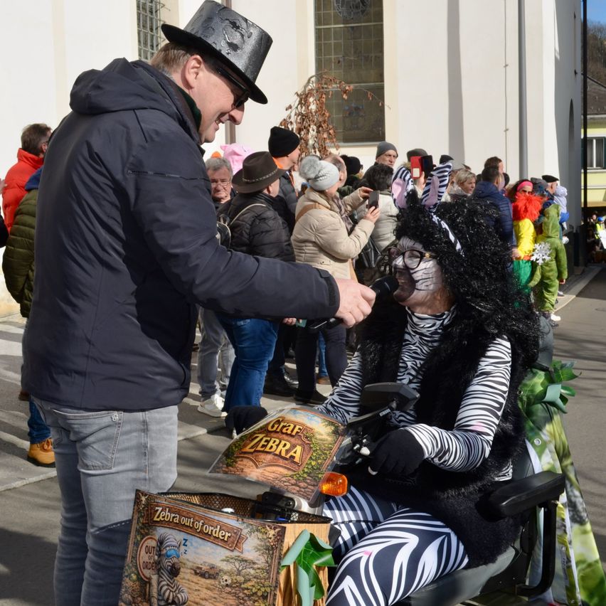 Ein Mann in einem Zylinderhut schüttelt die Hand einer Frau in einem Zebrakostüm in einer Menschenmenge während eines Festivals.