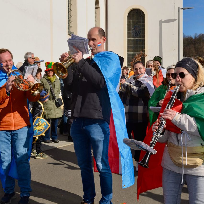 Eine Gruppe von Musikern in bunten Kostümen spielt Trompeten und Klarinetten vor einem Gebäude.