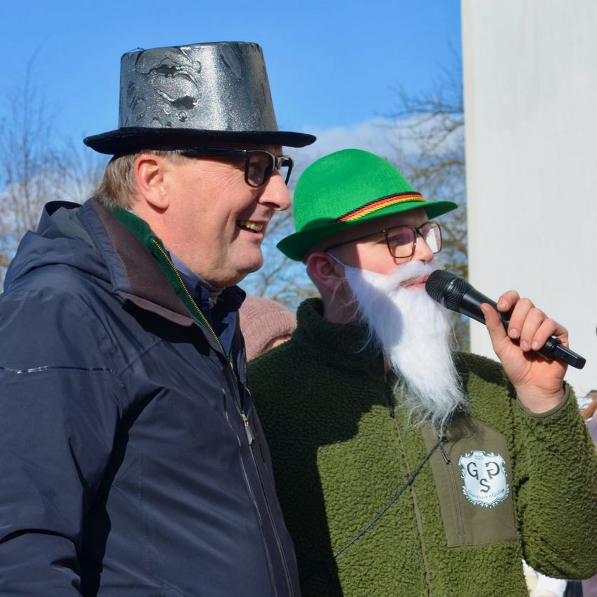 Zwei Männer stehen zusammen; einer in einem silbernen Hut und mit einer Brille, der andere in einem grünen Hut mit weißem Bart und Mikrofon.
