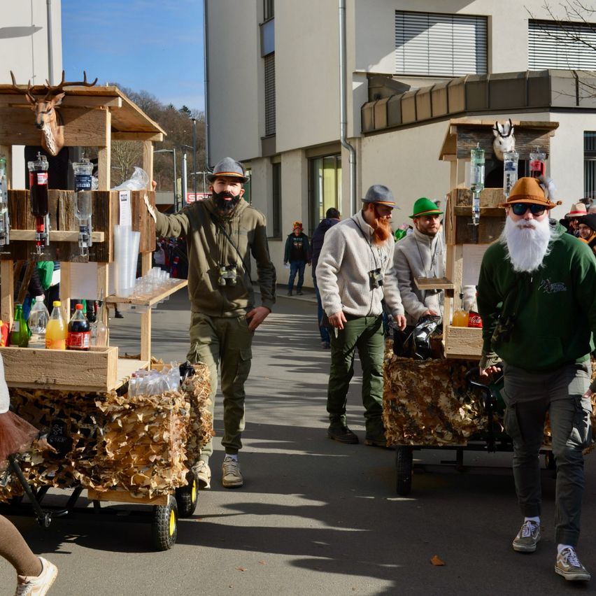 Mehrere Männer schieben Holzwagen die Straße hinunter, einer steht und hält einen Wagen. Sie tragen alle Hüte und Sonnenbrillen.