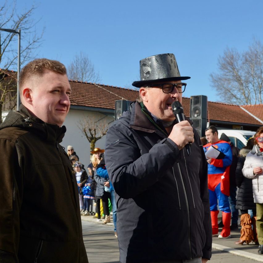 Ein Mann mit schwarzem Topfhut spricht in ein Mikrofon vor einer Menschenmenge an einem sonnigen Tag.