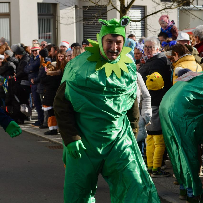 Ein Mann in einer Kermit-der-Frosch-Verkleidung steht in einer Menschenmenge, die Winterkleidung und Mützen trägt.