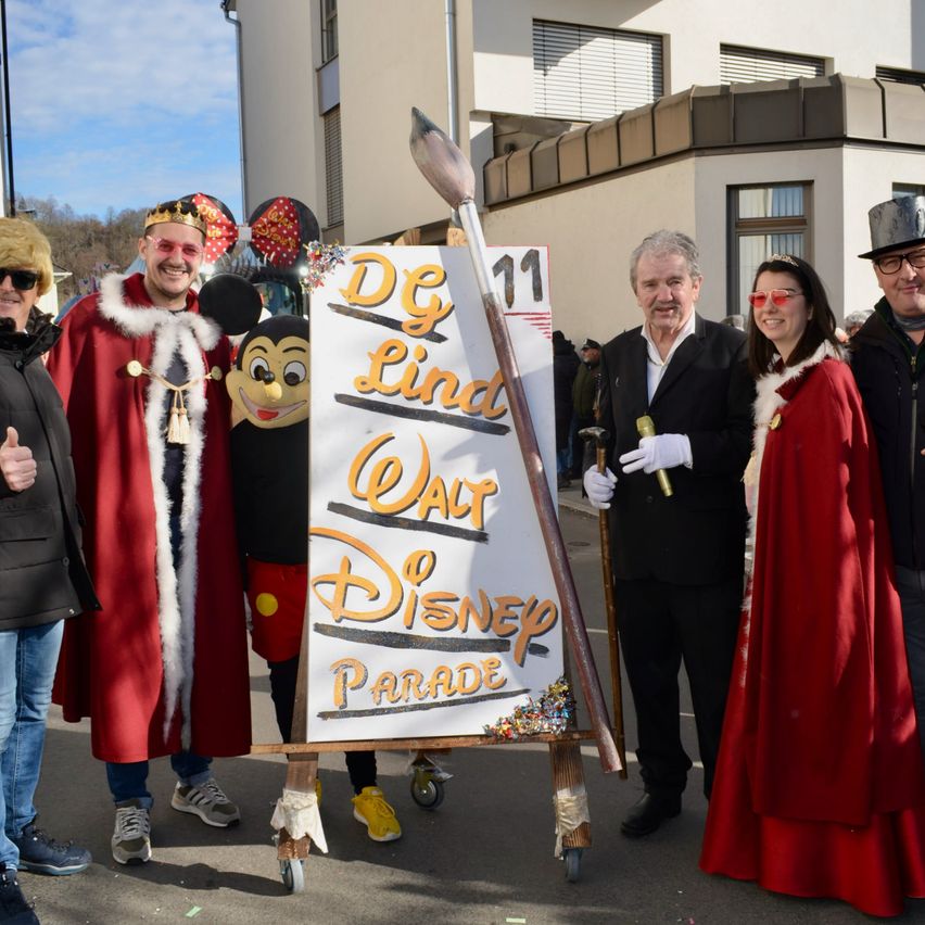 Gruppe von Menschen in Kostümen steht um ein Schild für die DG Linda Walt Disney Parade.