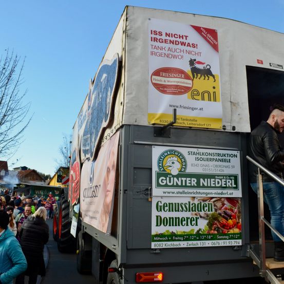 Ein Lastwagen zeigt eine Werbung für Friesinger Würste. Ein Mann steht auf den Stufen des Lastwagens. Viele Menschen stehen hinter dem Lastwagen.