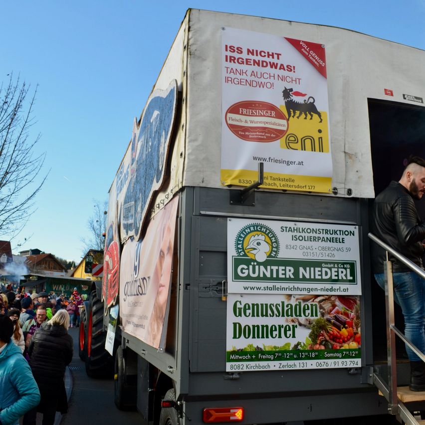 Ein Lastwagen zeigt eine Werbung für Friesinger Würste. Ein Mann steht auf den Stufen des Lastwagens. Viele Menschen stehen hinter dem Lastwagen.