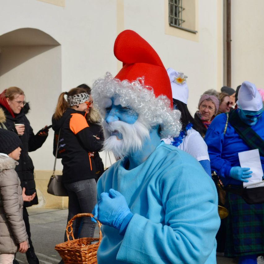 Eine Person in einem blauen Kostüm mit rotem Hut und weißem Bart steht vor einer Menschenmenge.