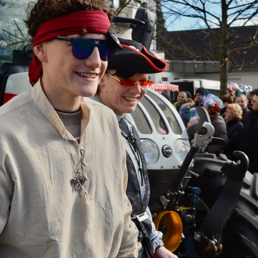 Zwei Menschen in mittelalterlichen Kostümen stehen vor einem Traktor bei einer Veranstaltung im Freien, mit einer Menschenmenge im Hintergrund.