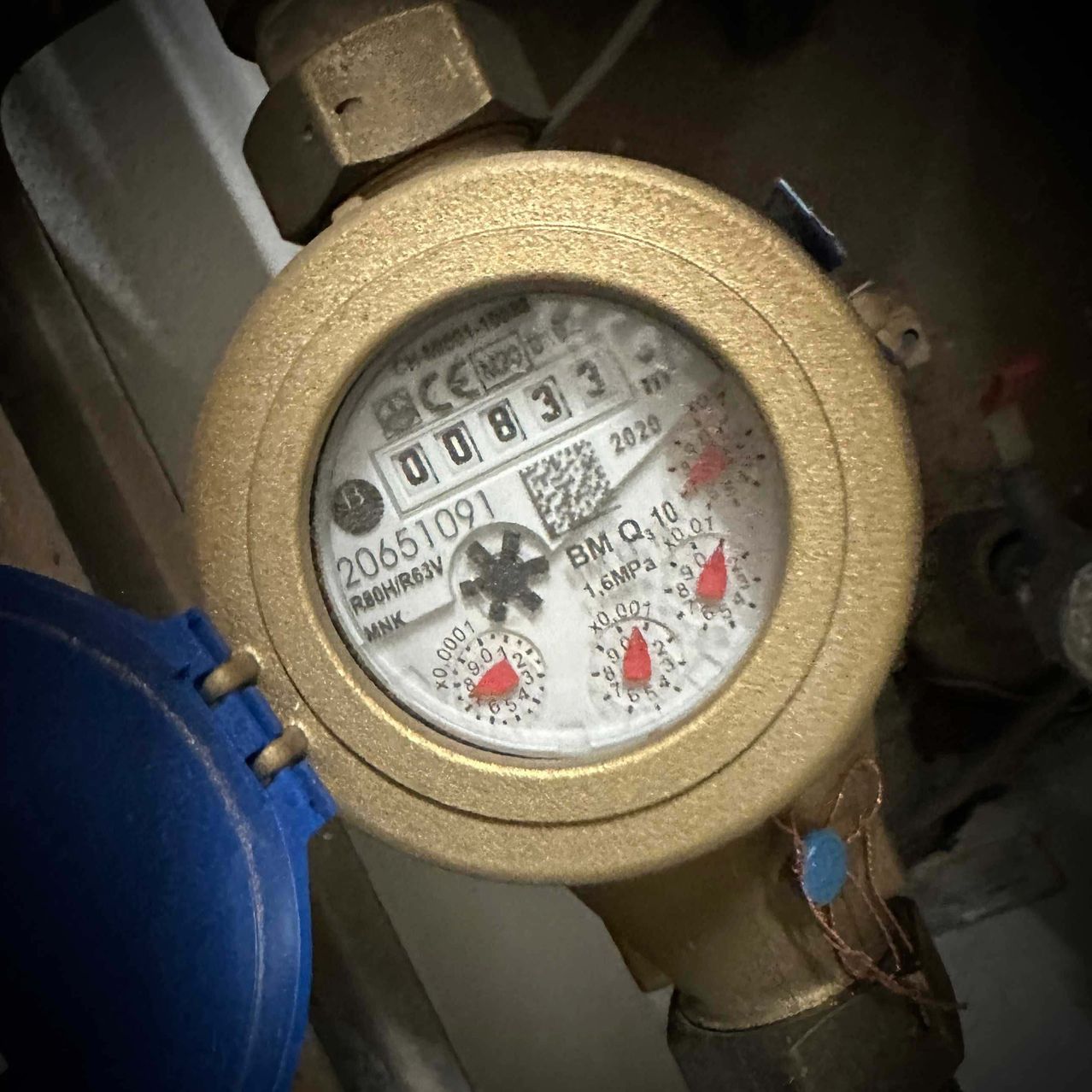 Nahaufnahme eines Wasserzählers mit Messinggehäuse, zeigt die Zahlen 20651091 und einen Barcode. Der Zähler liest 2020, mit zusätzlichen Details wie MNK, R80H/R63V und 1,6 MPa.