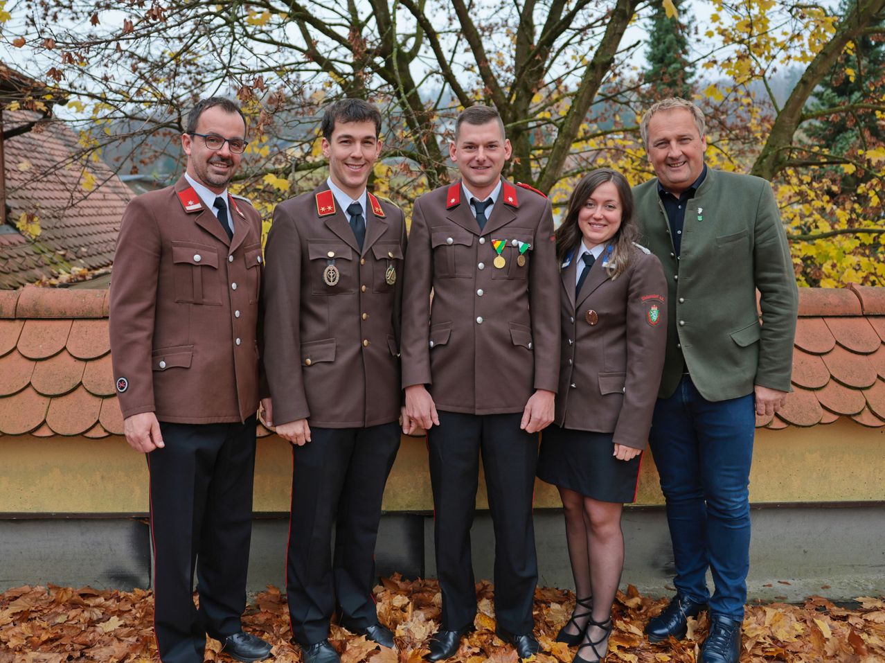 Fünf Personen in formeller Militäruniform posieren für ein Foto. Drei Männer und zwei Frauen, alle lächelnd, stehen zusammen vor einem Baum.