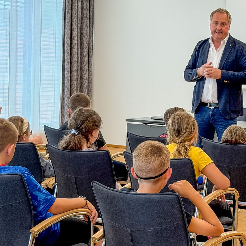 A man is standing in front of a group of children, possibly a teacher, giving a lecture in a classroom.