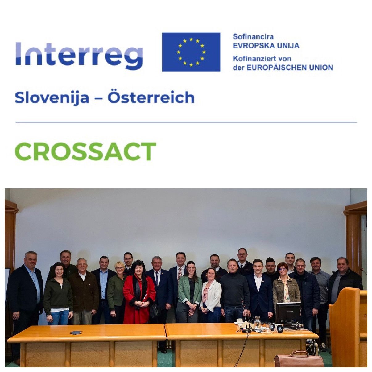 Ein Gruppenfoto von Menschen, die vor einem Schreibtisch stehen, beschriftet mit 'Interreg Slowenien-Österreich CROSSACT' mit der EU-Flagge und Logos.