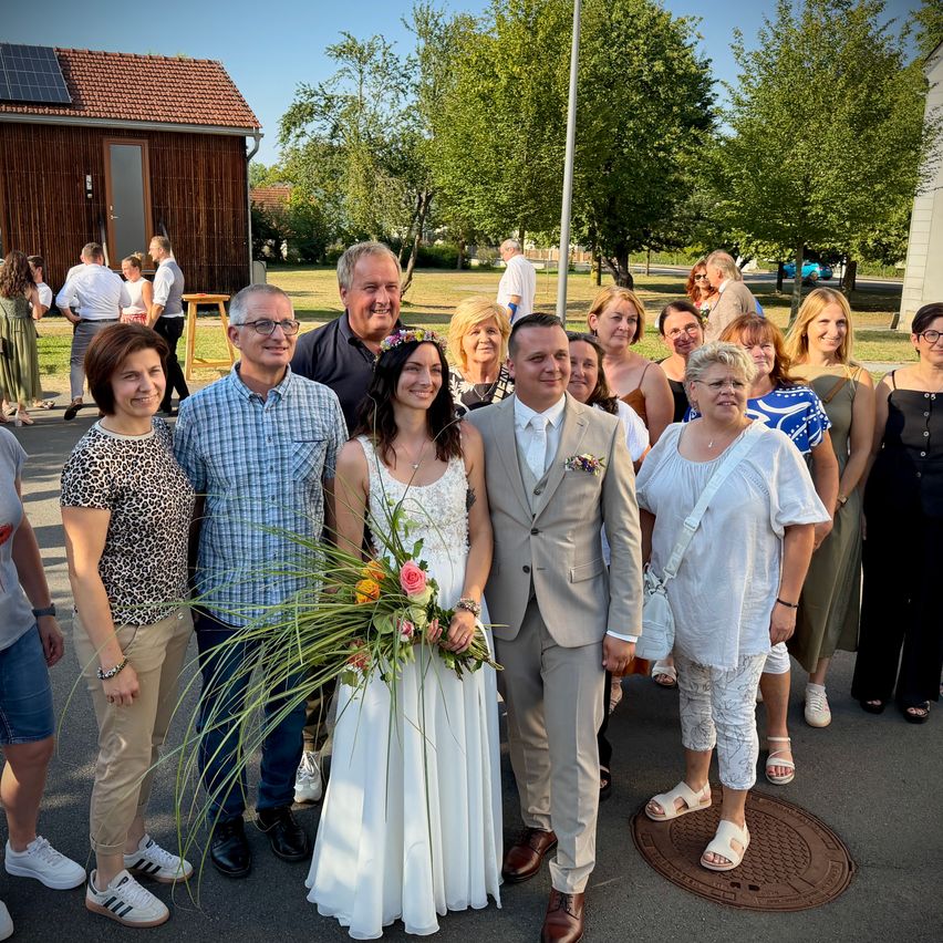 Eine Gruppe von Menschen, darunter ein Brautpaar, posiert für ein Foto vor einem Haus mit Solarmodulen auf dem Dach.