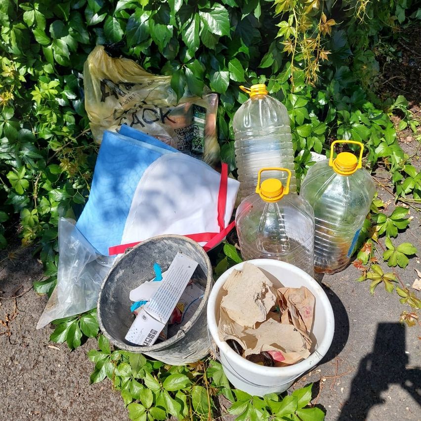 Ein Haufen Müll, bestehend aus Plastiktüten, Flaschen und einem Eimer mit verschiedenen Gegenständen, liegt auf dem Boden.