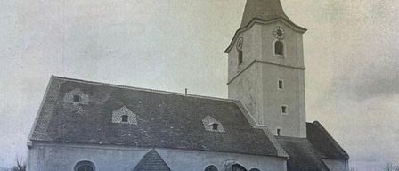 An old black and white photograph of a church with a tall steeple, clock, and a statue in front.