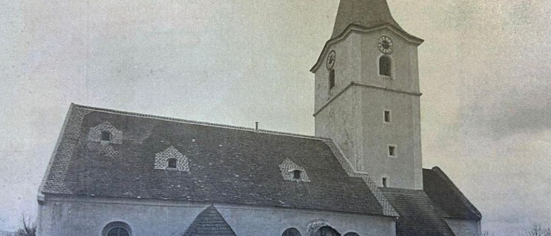 An old black and white photograph of a church with a tall steeple, clock, and a statue in front.