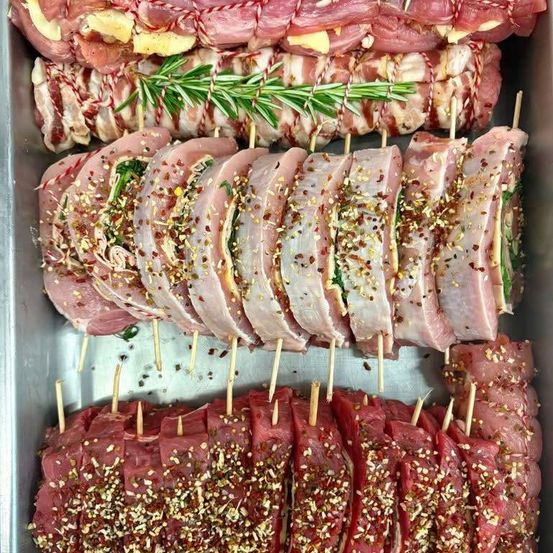 Ein Tablett mit aufgespießten Schweinelenden, jede in Speck und Rosmarin gewickelt, mit verschiedenen Gewürzen bestreut.
