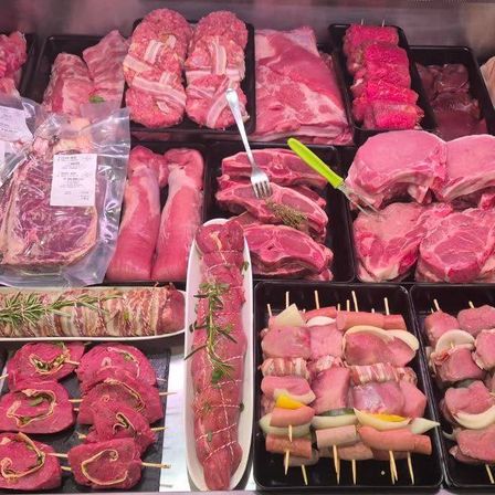 Eine Ausstellung verschiedener Fleischsorten, einschließlich Steaks, Würste und Kebabs, auf schwarzen Tabletts mit Rosmarin und anderen Kräutern angeordnet.