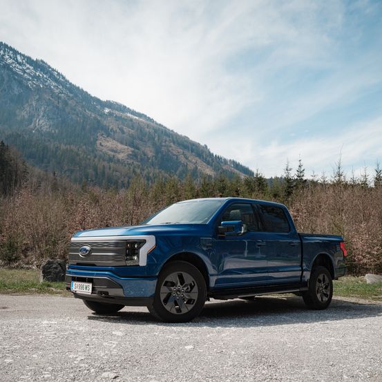 Ein blauer Ford F-150 Pickup-Truck, der auf Schotter geparkt ist, mit einem verschneiten Berg im Hintergrund.